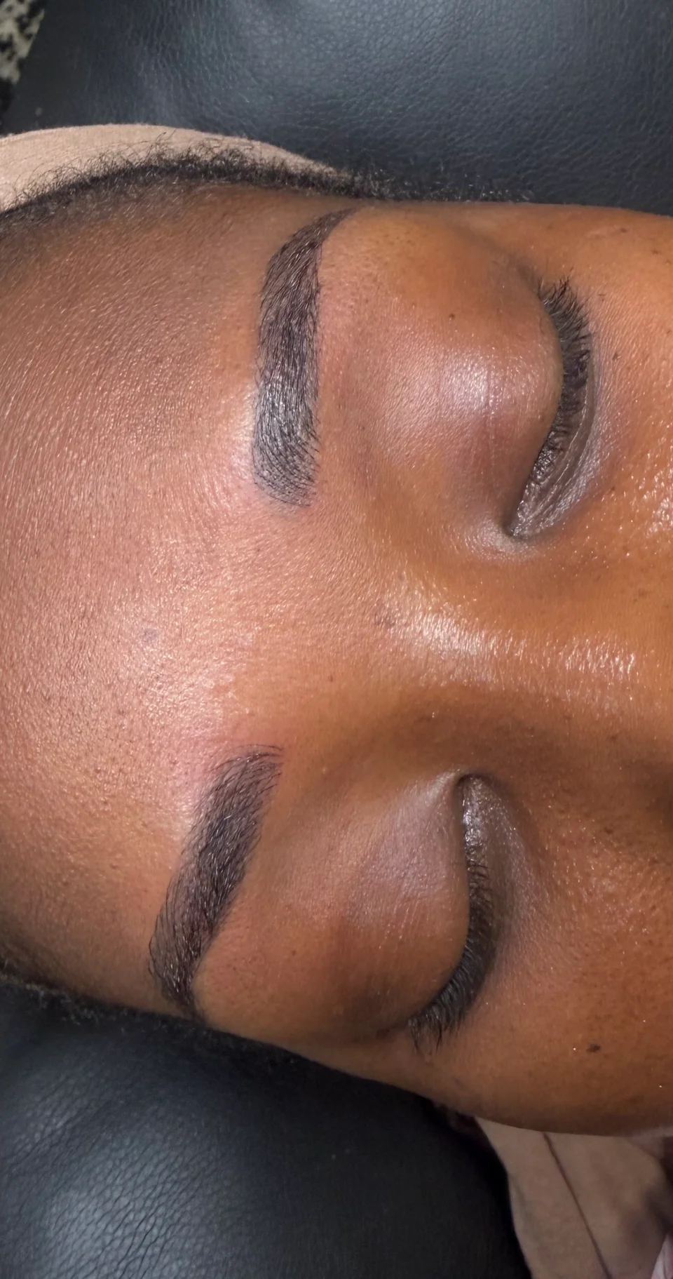 Close-up of both brows showing defined arches and fine strokes, with the client’s eyes closed.